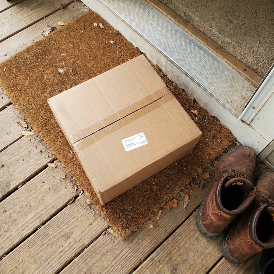 Plain brown cardboard box on a front porch doormat